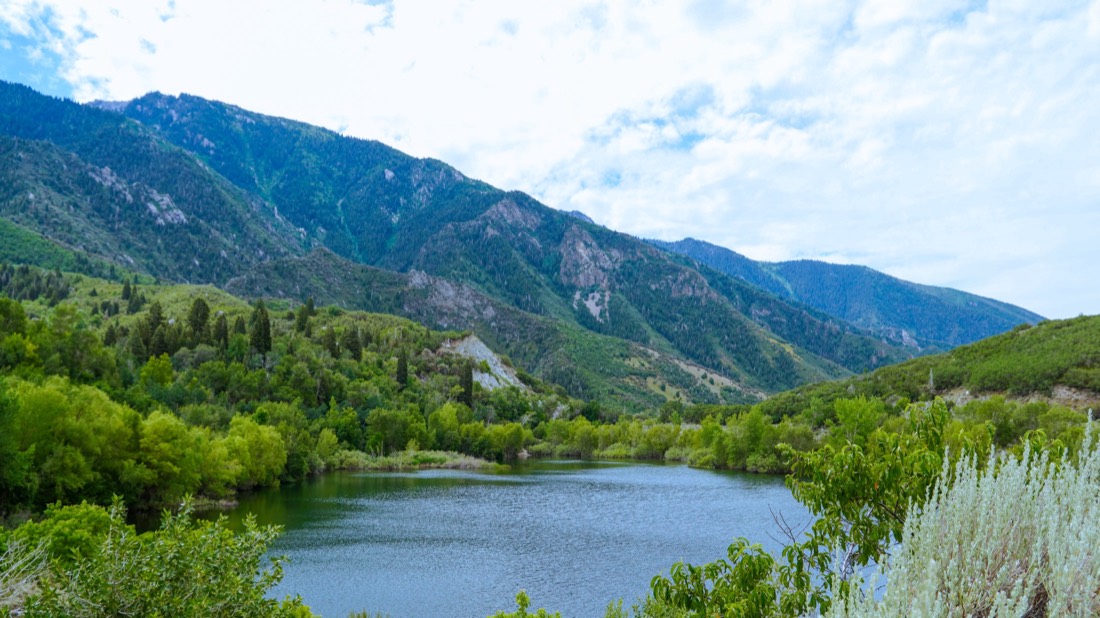 A calm mountain lake beneath green, sunlit slopes